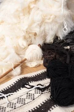Raw white and black wool surrounds wooden drop spindle on woven al sadu tex.. Stock Photos