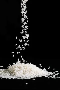 Raw white rice is falling on table. Pile of uncooked long rice on black Stock Photos