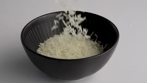 Raw white rice grains continuing to fill black bowl macro, FHD Stockbeeldmateriaal 341836096