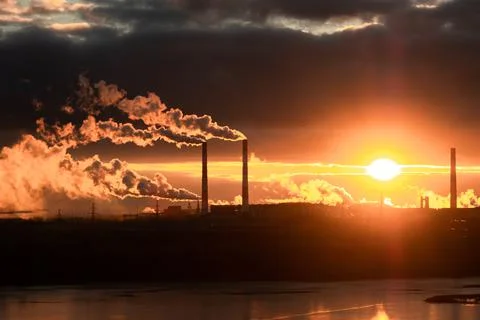 In the rays of the bright setting sun an enterprise with smoking chimneys Stock Photos