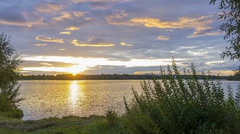 The rays of the dawn sun on the lake. Reflection of sunset clouds in the river Stock Photos