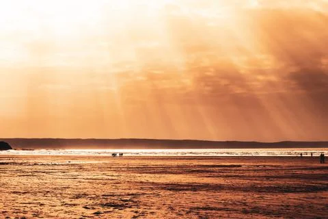 Rays of light and sunbeams shine down into a quiet sandy uk beach at sunset Stock Photos