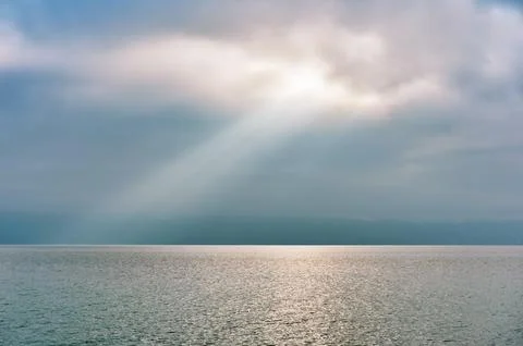 Rays of light falling through clouds on calm water surface Stock Photos