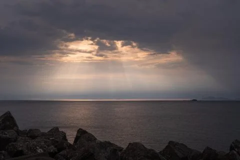 Rays of light shining through dark clouds on sea during sunset Stock Photos