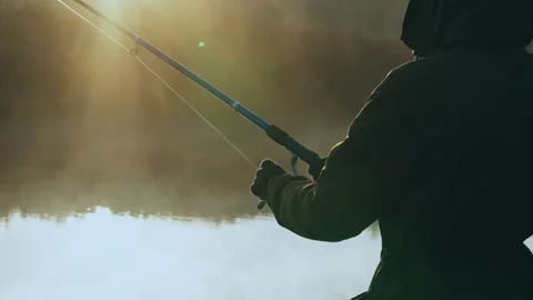 Rays of the rising sun light on man fishing at the riverbank Stock Footage 166686299