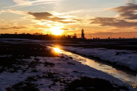 The rays of the setting sun are reflected in a small river on a winter even.. Stock Photos