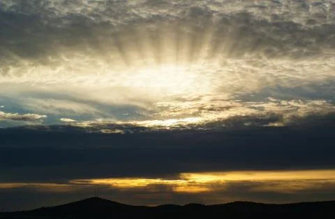 The rays of the setting sun behind the clouds. Stock Photos