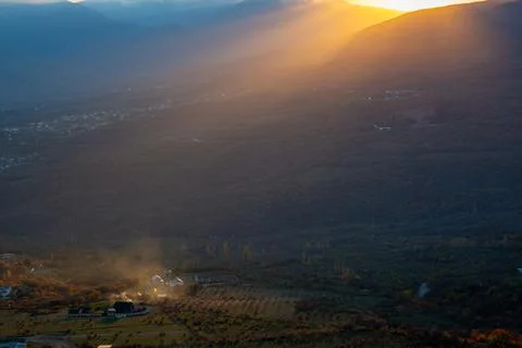 The rays of the setting sun illuminate the mountain valley from under blue cl Stock Photos
