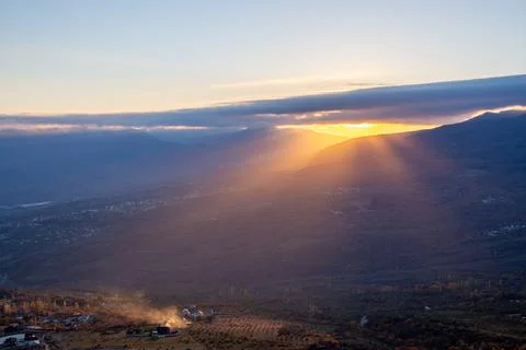 The rays of the setting sun illuminate the mountain valley from under blue cl Stock Photos