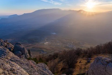 The rays of the setting sun illuminate the mountain valley from under blue cl Stock Photos
