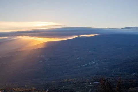 The rays of the setting sun illuminate the mountain valley from under blue cl Stock Photos