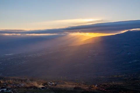 The rays of the setting sun illuminate the mountain valley from under blue cl Stock Photos