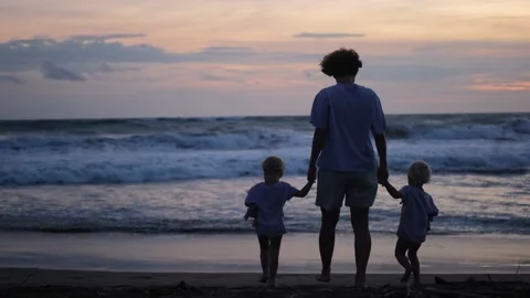 In the rays of the setting sun, a single mother leads two children to the water Stock Footage 175592175