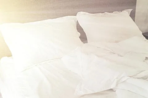 Rays of sun in bedroom, an empty bed, white pillow and blanket close up Stock Photos