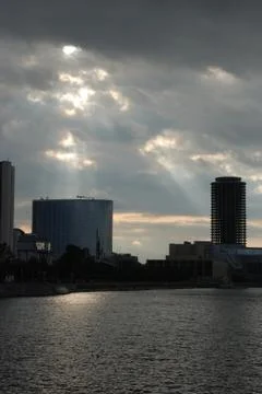 Rays of the sun coming through clouds over the buildings near the river Stock Photos