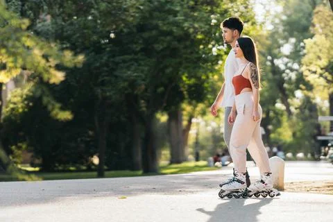 Rays of the sun illuminating two people skating in a park Stock Photos