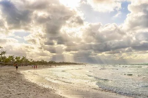 The rays of the sun make their way through the clouds over a deserted beach Stock Photos