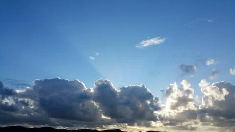Rays of the sun shine over dark clouds on the blue sky background Stock Photos