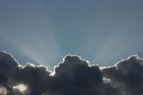 Rays of the sun shine over dark clouds on the blue sky background Stock Photos
