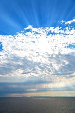 Rays from the sun in the sky above the cloud and above the water Stock Photos