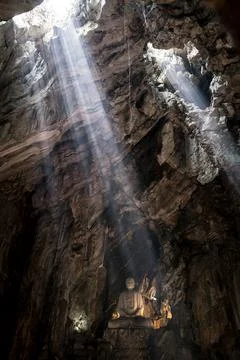 Rays of sunlight penetrate the cave ceiling to illuminate the stone buddha st Stock Photos