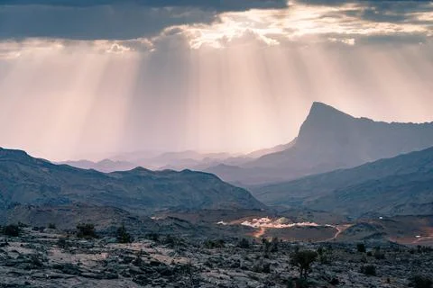Rays of sunlight shine through scattered clouds on a small arabian village in Stock Photos