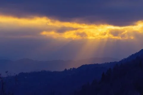 Rays of sunlight shining through clouds over dark landscape in the evening Stock Photos