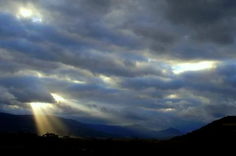 Rays of sunlight in the sky over the mountains at sunset Stock Photos
