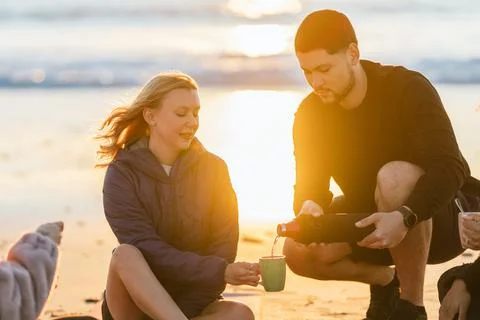 Rays of sunset illuminating a man serving tea to a women sitting on the beach Stock Photos