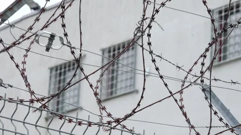 Razor wire and a tall security fence surround a white building with barred Stock Footage 318947903