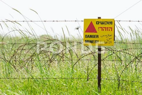 Razor wire guard fence and warning sign on mines field Stock Photos