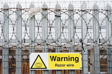 Razor wire warning sign on security fence at construction site Stock Photos