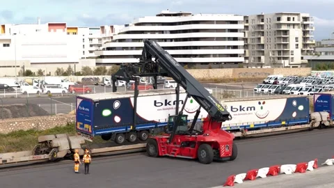 Reach stacker crane loading a BKM Logistics semi-trailer onto a specialized Stock Footage 337976501