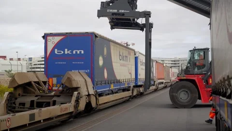 Reach stacker crane loading truck trailers onto specialized railway flatcars at Stock Footage 337975996