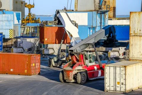 Reach stackers and cranes move containers near bulk carrier on sunny day Stock Photos