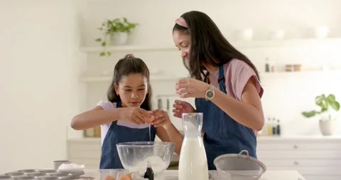 Reaching daughter cracking eggs while mother steadying bowl at home for baking, Stock Footage 342019383