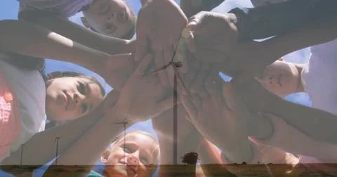 Reaching five kids stacking hands over lens in tops, watch on grassy plain with Stock Photos