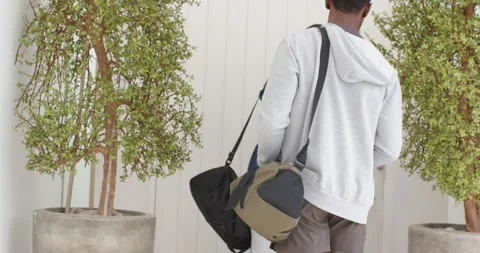 Reaching handle, father and son carrying duffel bags opening door into living Vidéo 341664867