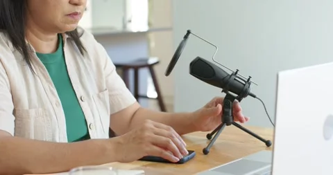 Reaching for mic, host adjusting mic mount at wooden table, typing on laptop Stock Footage 344340601