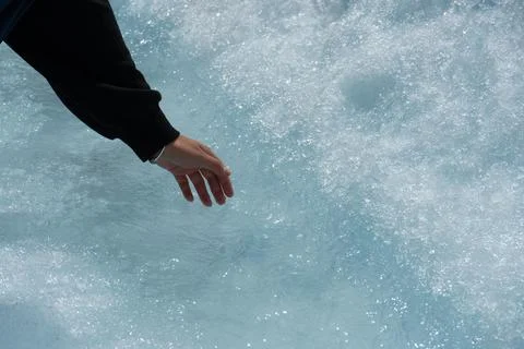 Reaching out to touch glacial ice and meltwater with gloved hand in sun Foto stock