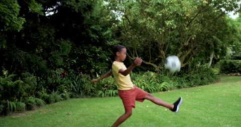 Reaching into shrubs, child is taking ball and practicing juggling in yard, Vídeos de archivo 342928931