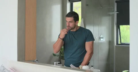 Reaching for toothpaste, man in teal tee picking toothbrush, brushing teeth at Vídeos de archivo 337026361