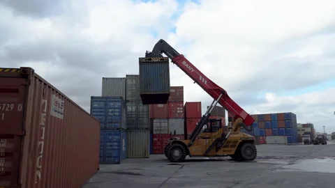 A reachstacker lifts a container against the backdrop of an open-air logistics  Stock Footage 148690728