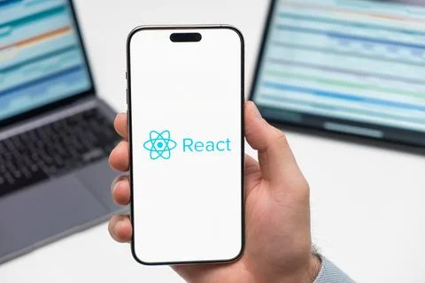React logo on the screen of smartphone in mans hand on the workplace background Stock Photos