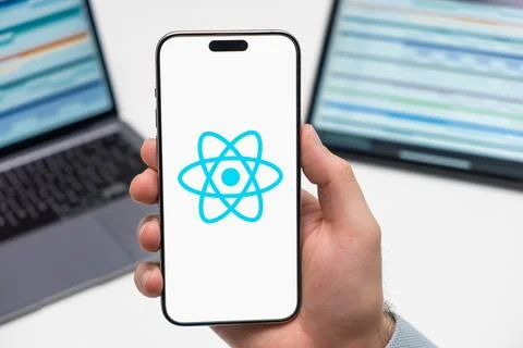 React logo on the screen of smartphone in mans hand on the workplace background Stock Photos