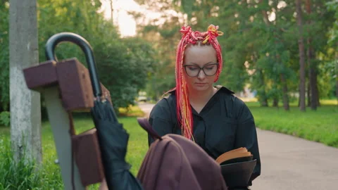 Reader with pink braids in park, sunset park scene with relaxed woman and book Stock Footage 329461925