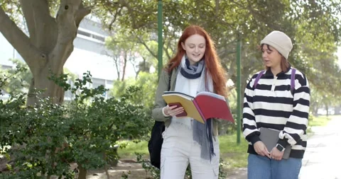 Reading binder passages, two female students walking campus path while Stock Footage 344325331