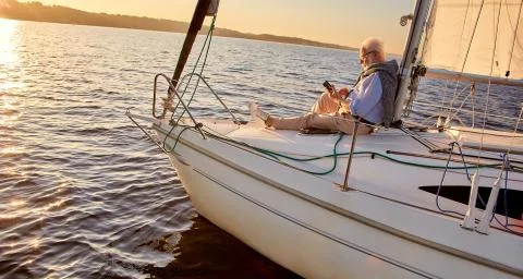 Reading on board. Side view of a relaxed senior man sitting on the side of Stock Photos