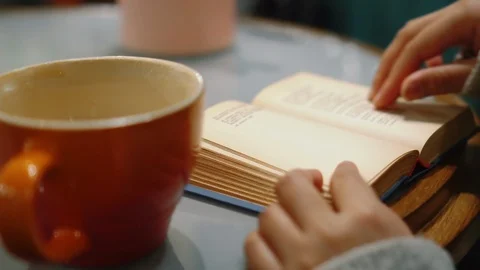 Reading book in cozy corner, cafe, with a cup of coffee or tea, turning pages. Stock Footage 126132114
