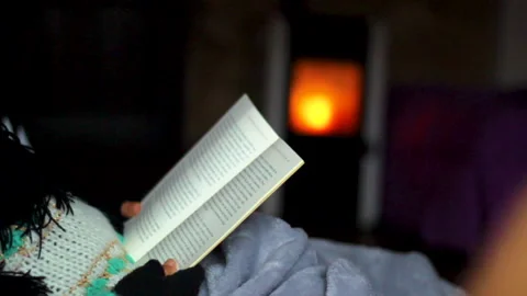 Reading book in darkness with fireplace by woman heand Stock Footage